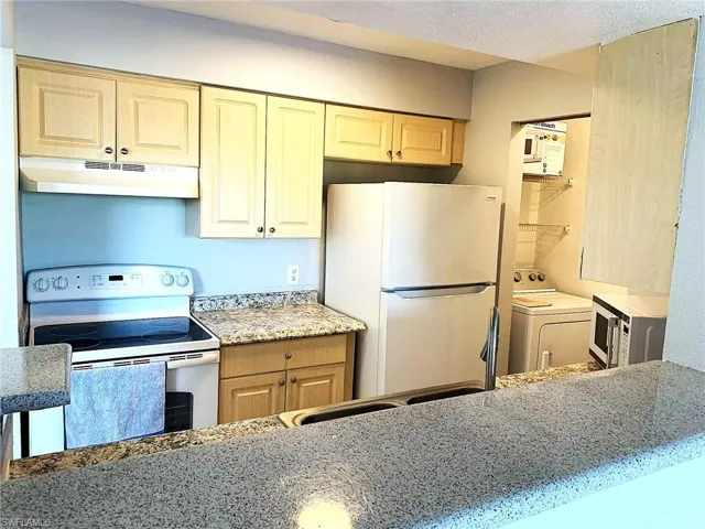 Kitchen with white appliances, washer / clothes dryer, under cabinet range hood, a textured ceiling, and light stone countertops