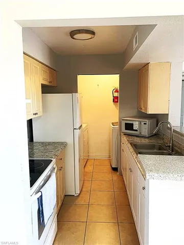 Kitchen with white appliances, washer and clothes dryer, light tile patterned floors, light brown cabinetry, and light stone counters