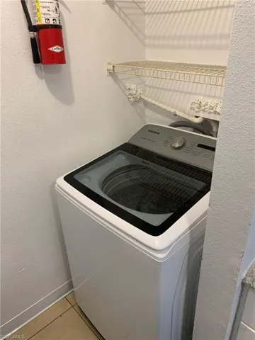 Laundry room featuring washer / clothes dryer, a textured wall, and light tile patterned flooring