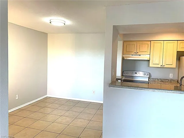 Kitchen with electric stove, light tile patterned floors, under cabinet range hood, a textured ceiling, and freestanding refrigerator