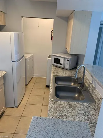 Kitchen with white appliances, separate washer and dryer, light tile patterned floors, and light stone counters