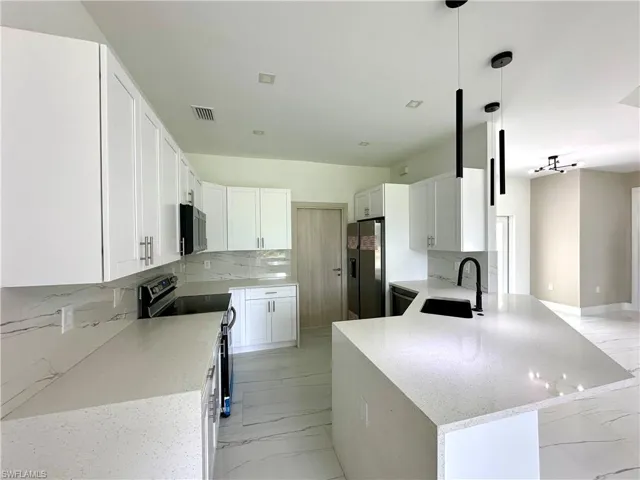 Kitchen featuring tasteful backsplash, light marble finish floors, light stone countertops, a peninsula, and white cabinetry