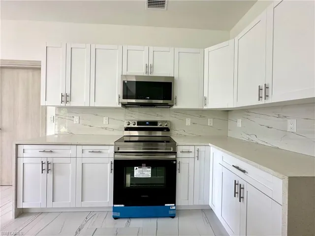 Kitchen with stainless steel appliances, white cabinetry, light stone counters, and decorative backsplash