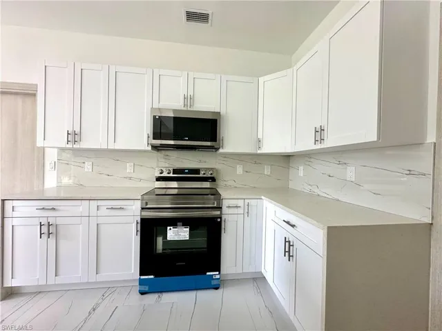 Kitchen with stainless steel appliances, white cabinetry, and light stone counters