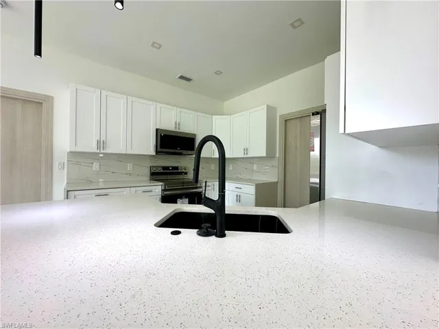 Kitchen featuring light stone countertops, white cabinetry, stainless steel appliances, and backsplash