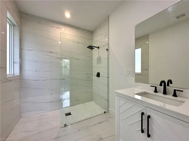 Full bathroom featuring vanity, a marble finish shower, and light marble finish floors