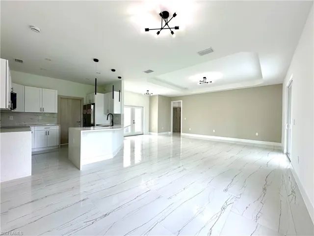 Kitchen with open floor plan, white cabinetry, a tray ceiling, light marble finish floors, and light stone counters