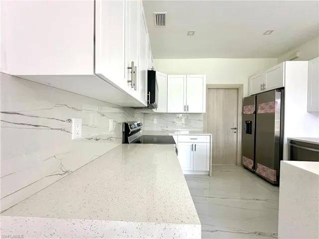 Kitchen with white cabinetry, stainless steel appliances, light stone counters, and tasteful backsplash