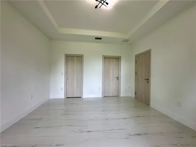 Unfurnished bedroom featuring a raised ceiling, light marble finish floors, and two closets