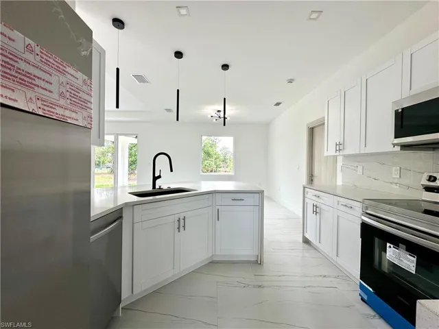 Kitchen with stainless steel appliances, white cabinets, light stone countertops, a peninsula, and decorative backsplash