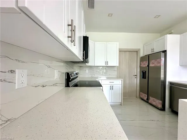 Kitchen with stainless steel appliances, light stone countertops, white cabinetry, and tasteful backsplash