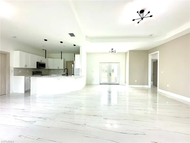 Unfurnished living room featuring french doors, light marble finish floors, and a raised ceiling
