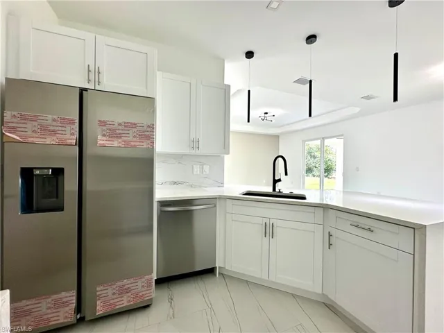 Kitchen featuring stainless steel appliances, decorative backsplash, white cabinetry, light stone counters, and pendant lighting