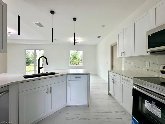 Kitchen with stainless steel appliances, light stone counters, white cabinetry, and pendant lighting