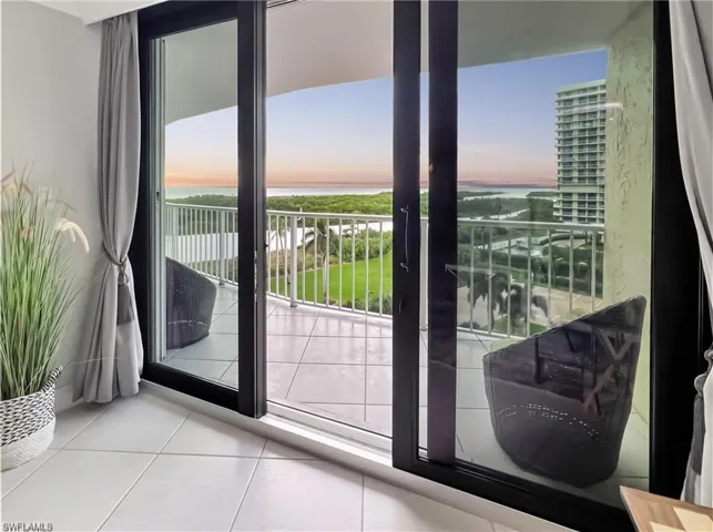 Large glass sliding doors, tiled private balcony, metal railing, and panoramic coastal scenery