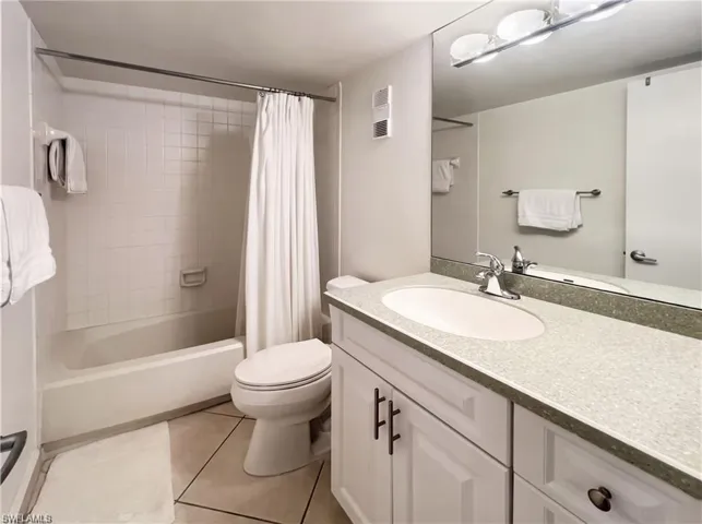 Bathroom featuring a vanity with a solid-surface countertop, an integrated oval sink, white cabinetry with dark hardware, a full-width wall mirror, and a tiled shower-tub combination