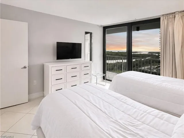 Floor-to-ceiling sliding glass doors, private balcony with metal railing, light-colored tile flooring, and neutral wall tones