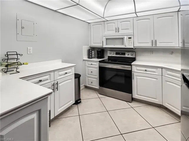 Kitchen featuring white cabinetry, solid-surface countertops, integrated stainless steel appliances, and tile flooring