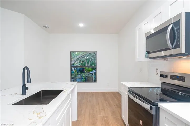 Kitchen featuring white cabinets, stainless steel appliances, light stone counters, and sink