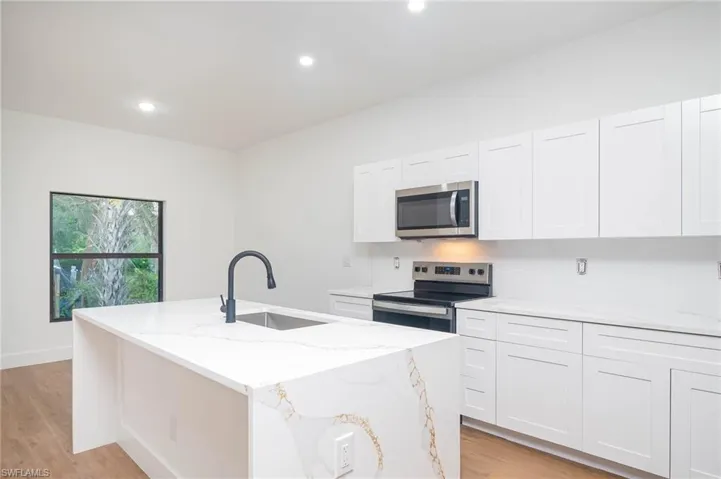 Kitchen with light stone countertops, sink, white cabinetry, stainless steel appliances, and a kitchen island with sink