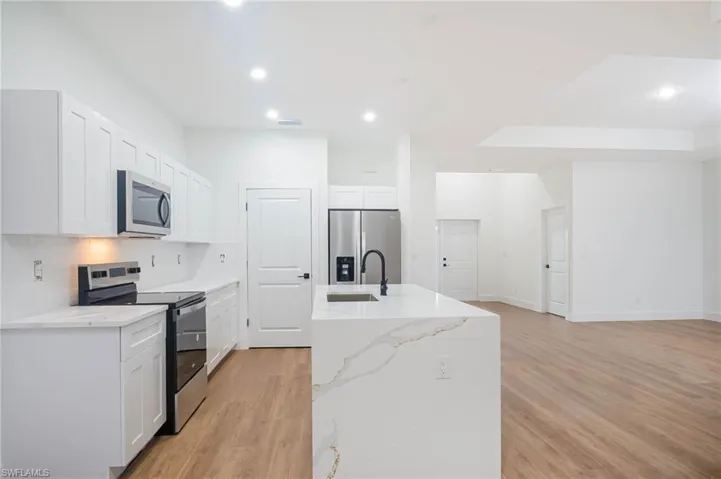 Kitchen featuring light stone counters, light hardwood / wood-style floors, a center island with sink, white cabinets, and appliances with stainless steel finishes