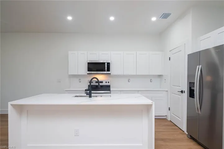 Kitchen with light stone counters, stainless steel appliances, a kitchen island with sink, sink, and white cabinets