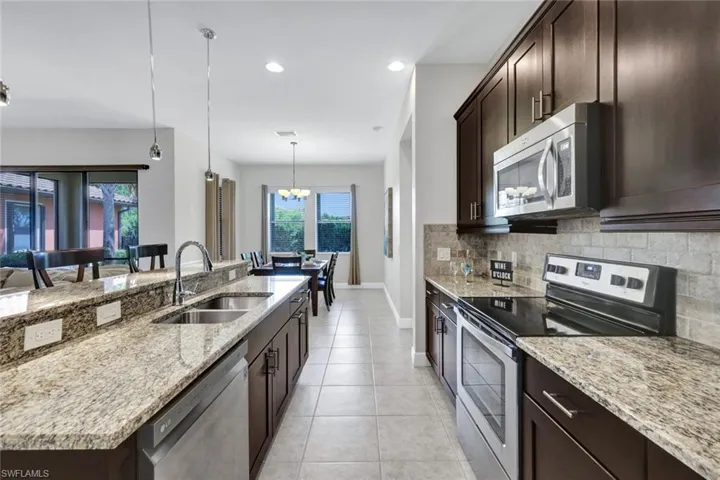 Kitchen with appliances with stainless steel finishes, a sink, decorative backsplash, dark brown cabinetry, and light stone counters