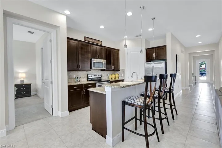 Kitchen with stainless steel appliances, dark brown cabinets, light tile patterned floors, light stone counters, and backsplash