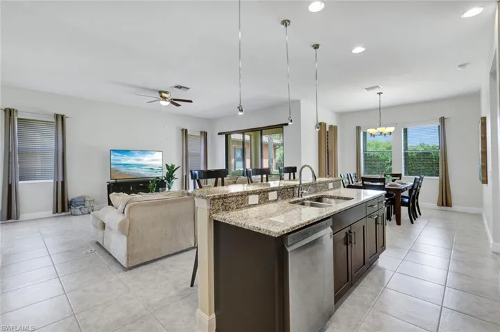 Kitchen featuring a sink, dishwasher, light tile patterned floors, open floor plan, and an island with sink