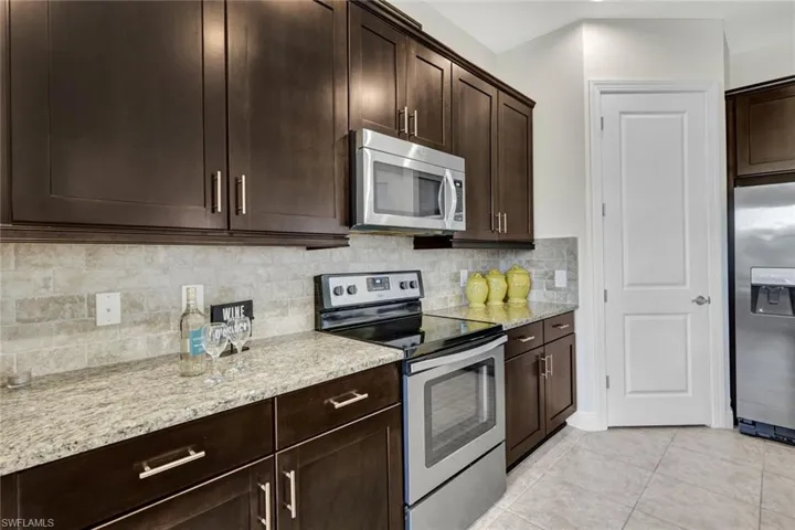 Kitchen featuring appliances with stainless steel finishes, light stone counters, dark brown cabinets, and tasteful backsplash