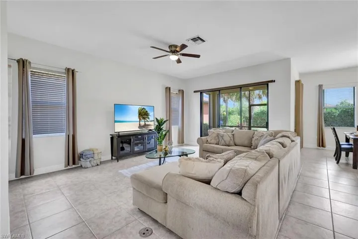 Living area featuring healthy amount of natural light, light tile patterned flooring, a ceiling fan, and baseboards