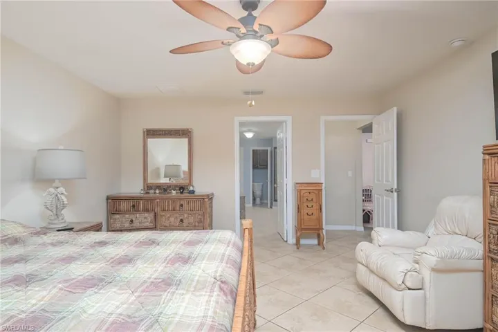 Bedroom featuring light tile patterned floors, ensuite bath, and ceiling fan