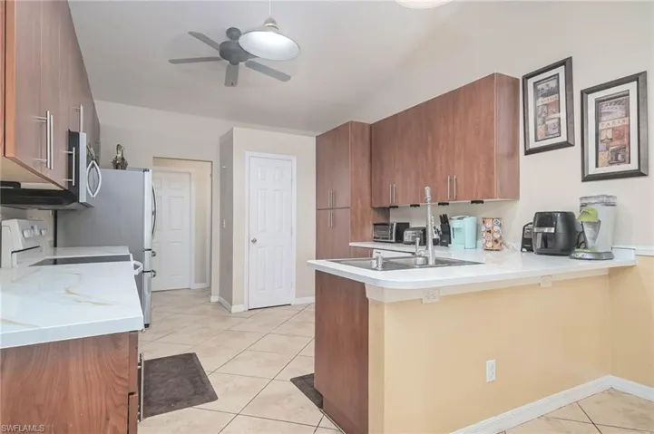 Kitchen featuring a peninsula, brown cabinets, ceiling fan, light tile patterned floors, and light countertops