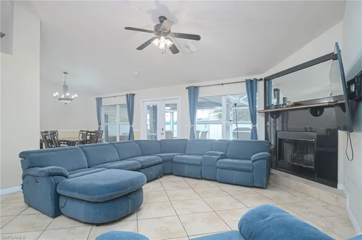 Tiled living room featuring vaulted ceiling, healthy amount of natural light, a chandelier, a ceiling fan, and french doors