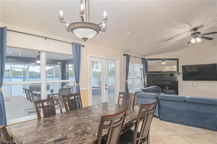 Dining room with lofted ceiling, a ceiling fan, light tile patterned flooring, a fireplace, and french doors
