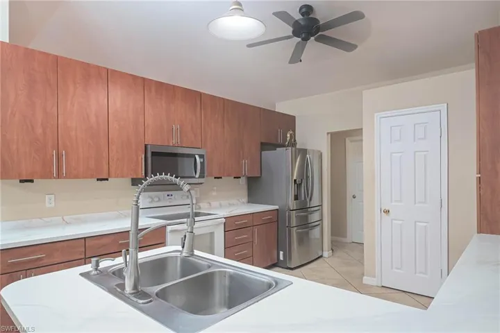Kitchen with stainless steel appliances, brown cabinetry, ceiling fan, light tile patterned floors, and light countertops