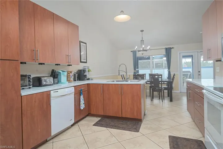 Kitchen with white appliances, a peninsula, a chandelier, light countertops, and light tile patterned floors