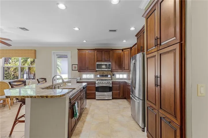 Kitchen featuring a kitchen bar, stainless steel appliances, sink, light stone countertops, and light tile patterned flooring
