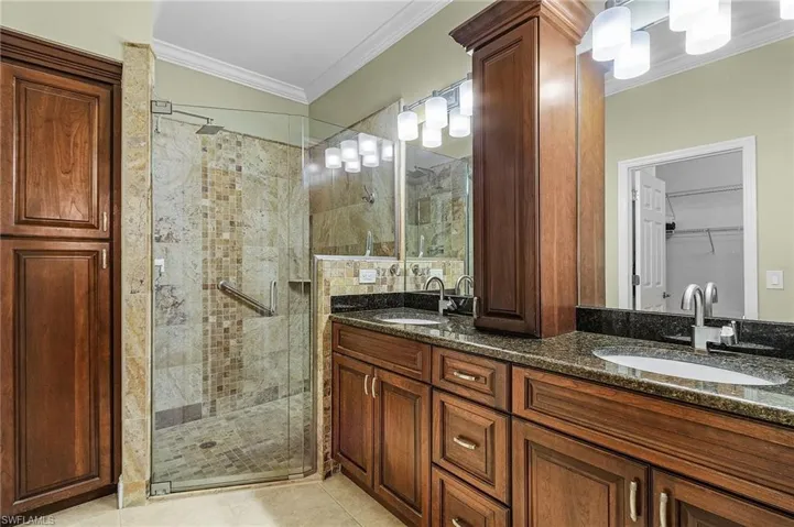 Bathroom featuring a shower with shower door, tile patterned floors, crown molding, and double vanity