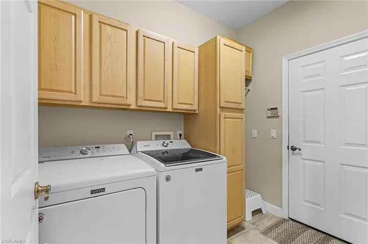 Clothes washing area featuring cabinets, washer and dryer, and light tile patterned floors