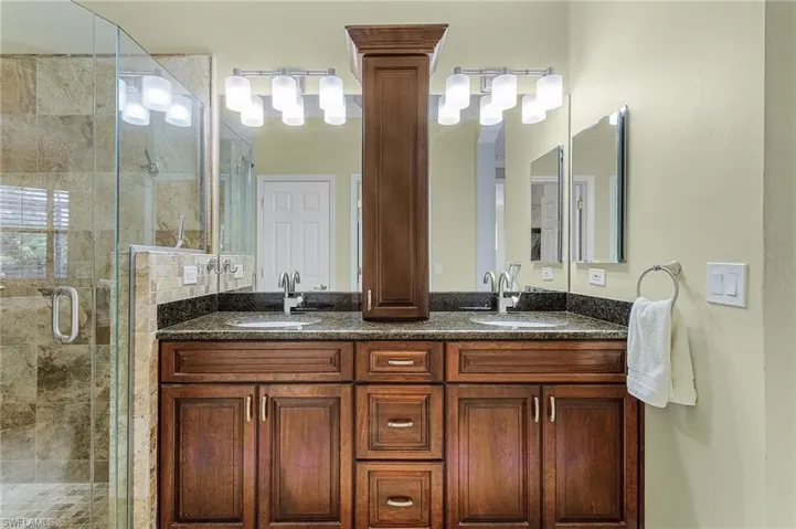 Bathroom featuring double vanity, a shower with shower door, and decorative columns