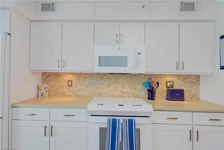 Kitchen featuring white cabinets, white appliances, and backsplash