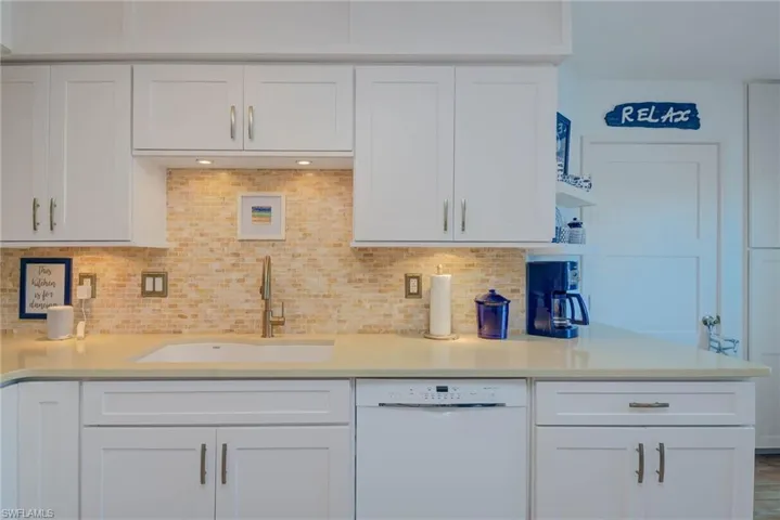 Kitchen with white dishwasher, white cabinetry, and sink