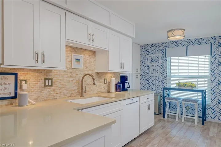 Kitchen with tasteful backsplash, white dishwasher, sink, light hardwood / wood-style floors, and white cabinetry