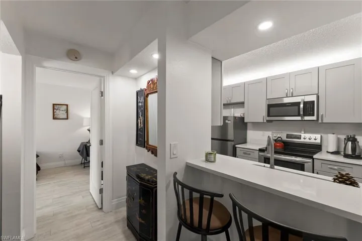 Kitchen featuring a breakfast bar, gray cabinetry, stainless steel appliances, light wood-style floors, and a peninsula