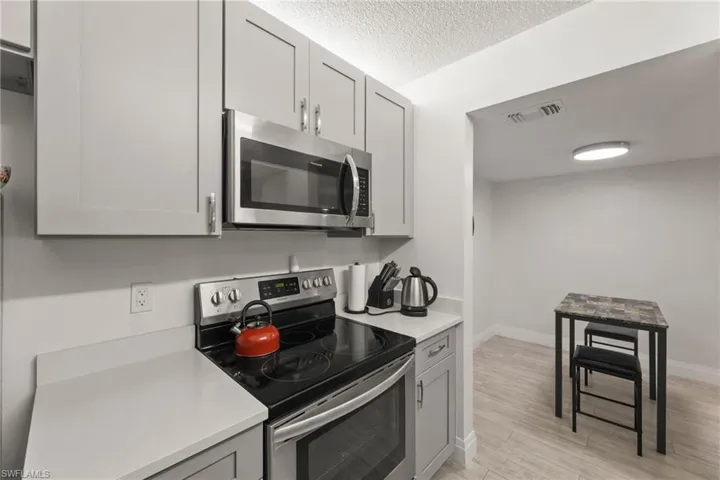 Kitchen with stainless steel appliances, gray cabinetry, light wood-style flooring, and a textured ceiling