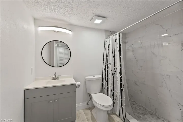 Bathroom featuring vanity, a stall shower, a textured ceiling, and light wood-style floors