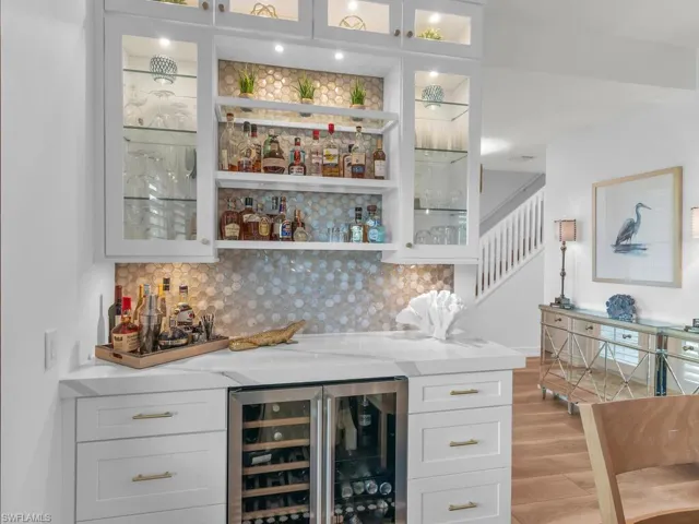 Bar with decorative backsplash, light stone counters, beverage cooler, light hardwood / wood-style floors, and white cabinetry