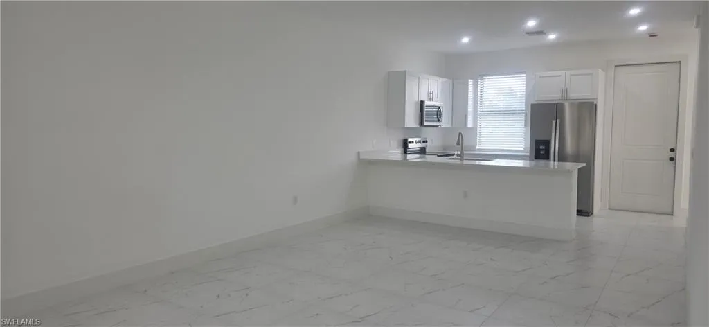 Kitchen with light marble finish floors, appliances with stainless steel finishes, a peninsula, white cabinetry, and recessed lighting