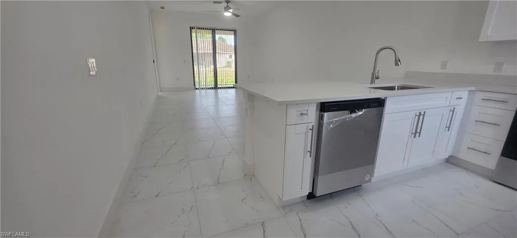 Kitchen featuring light marble finish flooring, stainless steel dishwasher, white cabinets, a peninsula, and light stone countertops